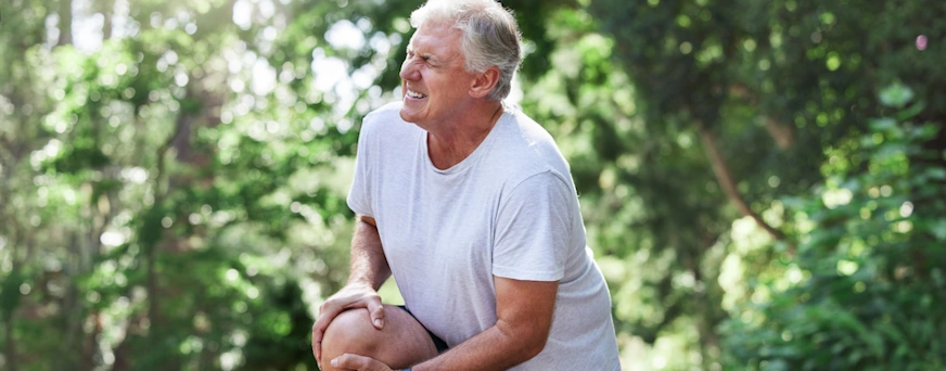 Life Assure Senior Experiencing Knee Pain In Park Hero